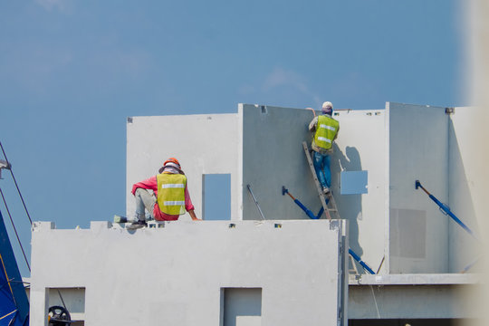 Construction worker are installing the precast concrete wall, orange safety helmet and green vest.