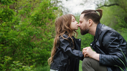Modern stylish family walking in the park. Daughter hugs and kisses dad.Time together. Family look. Urban casual outfit.