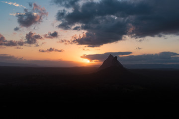 As the sun sets over the Glass House Mountains, the clouds are painted with beautiful yellows and oranges and the mountains in the foreground are turned into striking black silhouettes