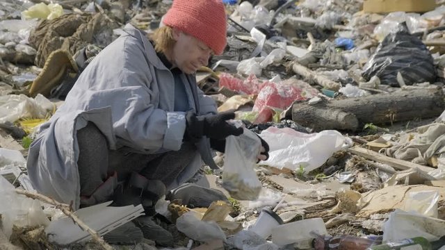 homeless man eats at city dump. bum digs in package of waste in garbage.