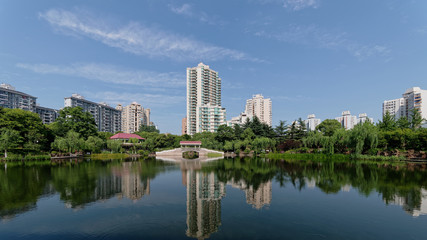 Landscape of Shanghai Quyang park, Chinese traditional bridge and green willow trees along peaceful lake, modern residential building and blue sky background.