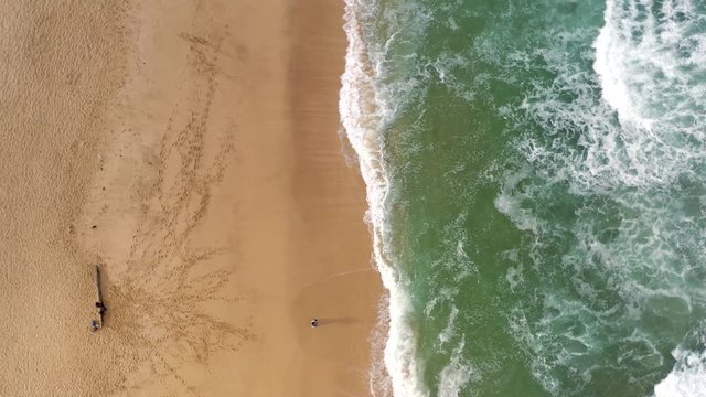 Drone rotation over sandy seashore with lonely fisherman. Aerial anticlockwise view of amazing sand beach with waves and turquoise blue water.
