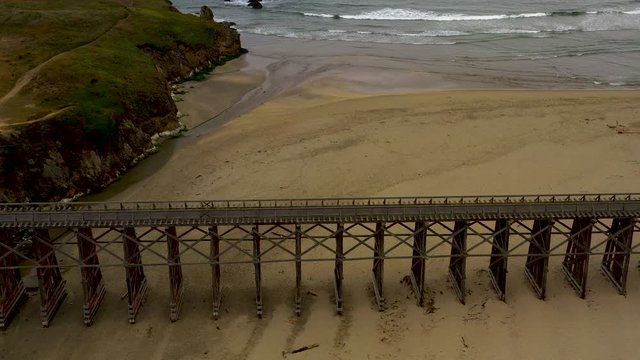 Aerial Panoramic Tilt of Pudding Creek Trestle, Front Bragg, California. Drone view of historical bridge on sand beach with ocean waves in a cloudy day.