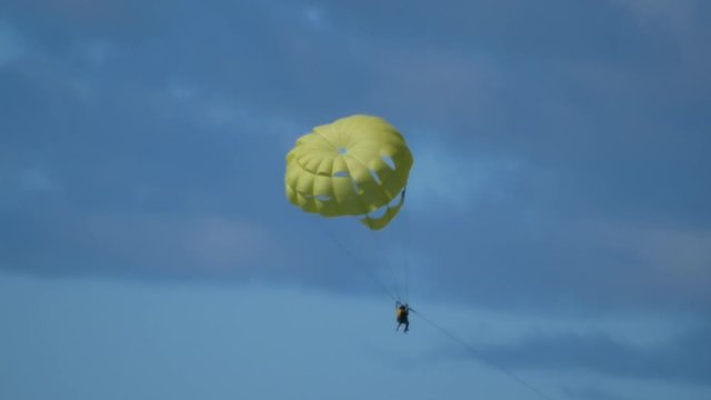 A couple doing parasailing descends hunged up a yellowish parachute.