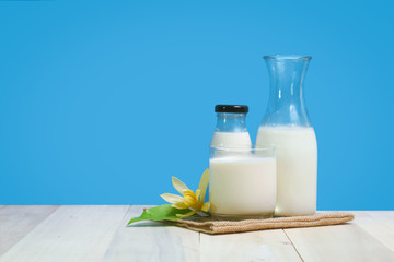 A bottle of rustic milk and glass of milk on a wooden table on a blue background