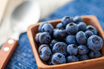 Blueberries in a wood bowl on top of blue and white napkin with a spoon