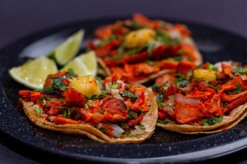 Tacos al pastor de carne de puerco con cilantro, cebolla y piña montados sobre un plato negro