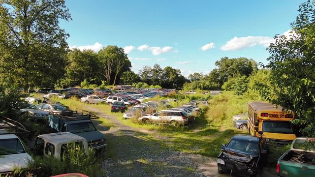 Low aerial pan left of junkyard full of wrecked cars and school bus on sunny summer afternoon