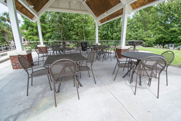 An empty pavilion filled with outdoor metal park tables and chairs during a sunny day outside 