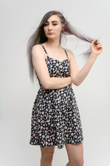 Full length studio portrait of a pretty student girl with long beautiful hair in a beautiful color dress on a white background. He stands straight, smiles, shows with his hands.