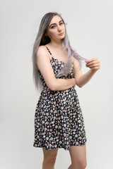 Full length studio portrait of a pretty student girl with long beautiful hair in a beautiful color dress on a white background. He stands straight, smiles, shows with his hands.