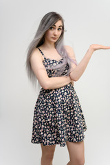 Full length studio portrait of a pretty student girl with long beautiful hair in a beautiful color dress on a white background. He stands straight, smiles, shows with his hands.