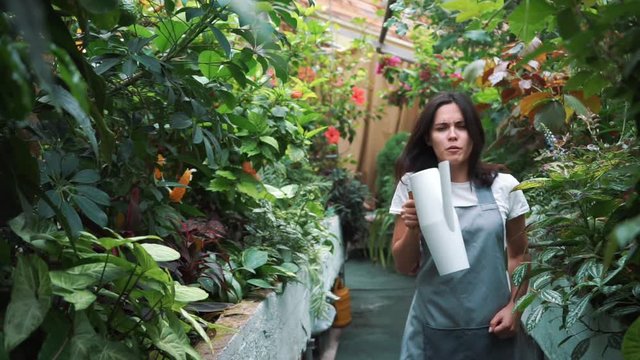 A beautiful girl in an apron dancing in a greenhouse. Florist happy, dancing and laughing.