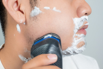 Close up of a young man shaving with electric razor.
