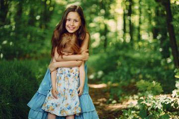 little beautiful girl with her older sister in a blue dress dressing up in a large sunny forest