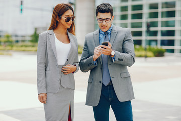 Handsome businessman in a city. Businessman in a glasses. Business couple in a summer city. Man and woman standing with phone. Pretty girl in a dress with her parther.