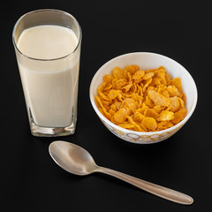 Cornflakes with milk in bowl with milk glass isolated on black gray background, a delicious dietary breakfast cereal.