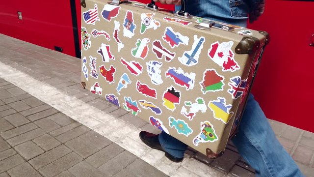 passenger is on the platform of the station with a suitcase with stickers from different countries in his hand.