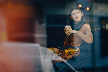 brunette girl sitting at a caffe drinking a hot beverage while looking out the window