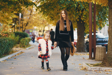 young beautiful long-haired mother in black dress walks with a little stylish daughter in the autumn city