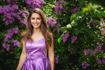 Pretty girl in purple dress posing in the blooming park. Spring trees and bushes