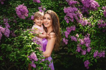 Mother and her child enjoy the early spring. Blooming lilac trees at background