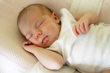 Cute newborn baby is sleeping on her bed.