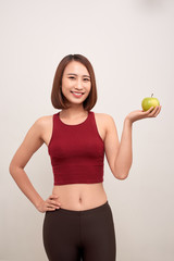 Fitness woman eating apple wearing measuring tape. Fit sporty multicultural Asian / Caucasian female fitness woman isolated on white background. - Image
