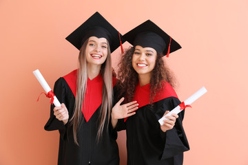 Young students in bachelor robes on color background