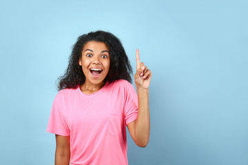 Excited young African-American woman with raised index finger on color background