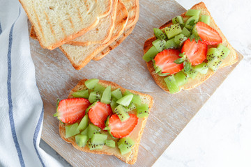 Tasty sandwiches with kiwi and strawberry on wooden board