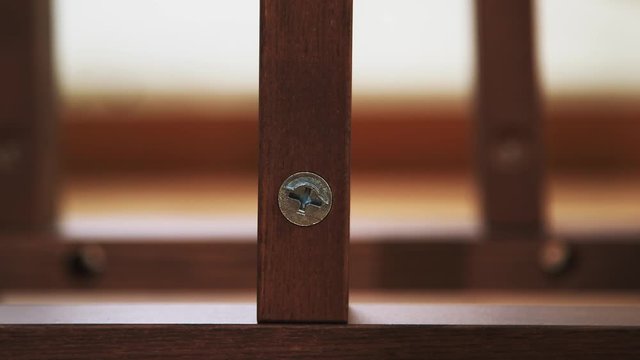 Hand inserts screw into hole in shelf. Large metal screw put into hole in wooden furniture. Finger pushes it in. Close up, frontal view.
