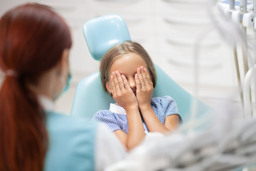 Little girl closing her eyes while feeling scared of dentist