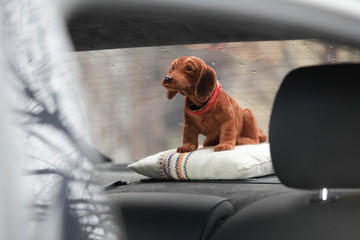 brown bobble head dog is sitting in the parcel shelf of a car - obrazy, fototapety, plakaty