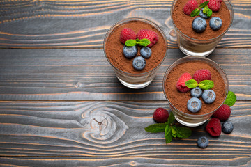 Classic tiramisu dessert with blueberries and strawberries in a glass cup on wooden background