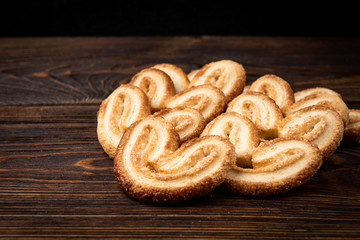 Palmier cookies or puff pastry ears on dark wooden background.