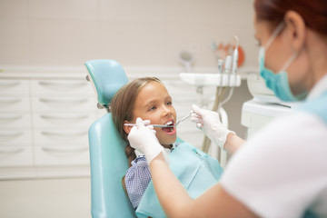 Child dentist wearing mask and gloves examining cute girl