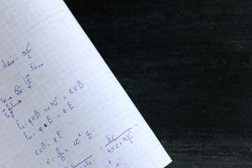 copybook abstract with formulas on black chalkboard background. solving problems in physics