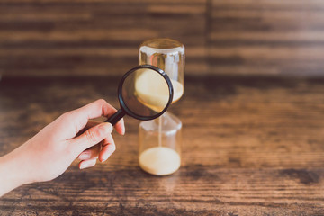 hand holding magnifying glass analyzing time passying by with an hourglass,