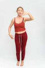 Full length studio portrait of a pretty young happy blonde woman in a tracksuit on a white background. He smiles, talks, shows with his hands, moves, shows emotions.