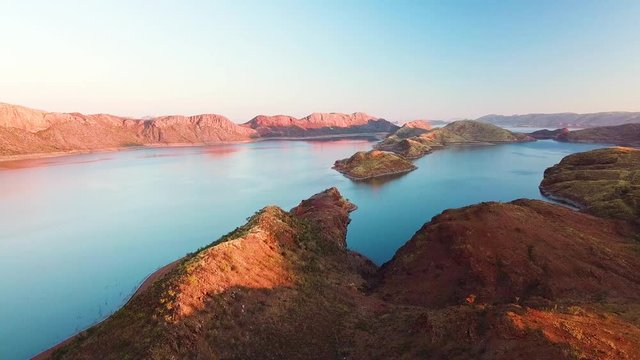 Aerial tracking shot of spectacular lake and arid mountains at dusk. Lake Argyle, Australia.