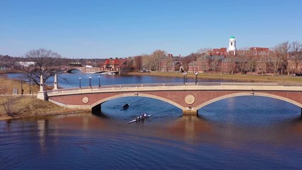 Aerial over the John W. Weeks Footbridge reveals Harvard University campus on the Charles River with rowing crew.