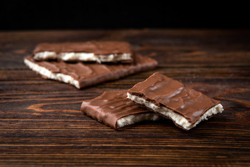Chocolate bar with coconut filling on dark wooden background.