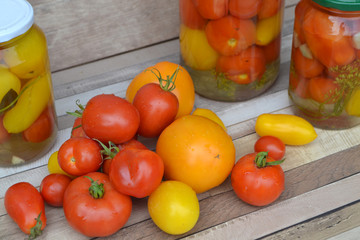 Red and yellow small marinated tomatoes in a transparent glass jar on shabby rustic table with fresh tomatoes