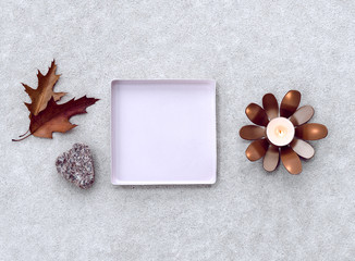 Composition with empty square metal tray, candlelight and maple leaves.