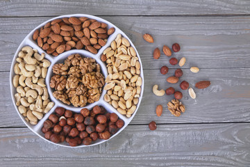 Nuts are part of a healthy diet . Set of nuts - walnut , cashew , peanuts , hazelnuts , almonds on a plate divided into portions . on a grey wooden background.