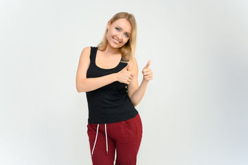 Studio knee-length portrait of a pretty beautiful young happy blonde woman on a white background in a black t-shirt and red trousers. Smiling, talking, showing emotions.