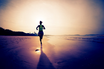 Sporty fitness woman runner running on sunrise beach