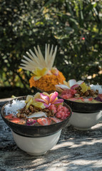 smoothie bowl in a coconut shell plate with with strawberries, chia seeds, banana, granola, flower on wooden background. Green tropical leaves background