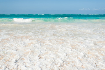 Beautiful sea foam at sandy beach of Punta Cana with azure water of Atlantic ocean on the background